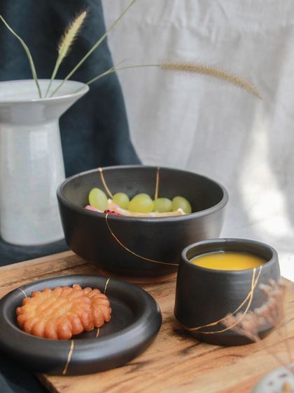 A breakfast or snack set from the 'Celebrations' collection, featuring a black bowl, plate, and cup with gold accents, blending style with everyday function.