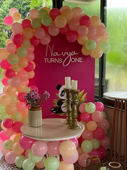 A chic first birthday corner with a balloon arch in shades of pink, peach, and mint green. The custom backdrop features a cute panda graphic for a modern and sweet touch.