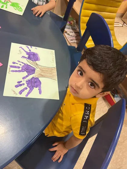 This little boy is proudly showing the family tree he made with his handprints. It's a beautiful and personal art project that helps children understand the concept of family in a creative way.