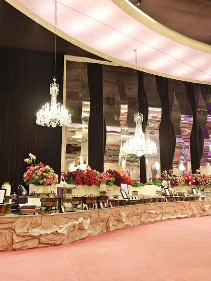 A long shot of a magnificent, curved buffet table under sparkling crystal chandeliers, demonstrating the scale and elegance of our food presentation.