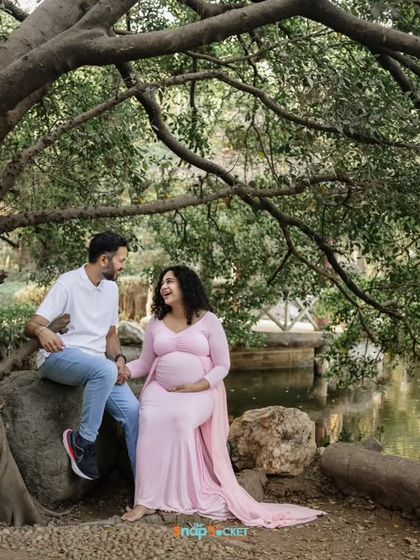 A beautiful, candid moment under a large tree. The natural setting provides a peaceful and romantic atmosphere for this couple's maternity portrait.