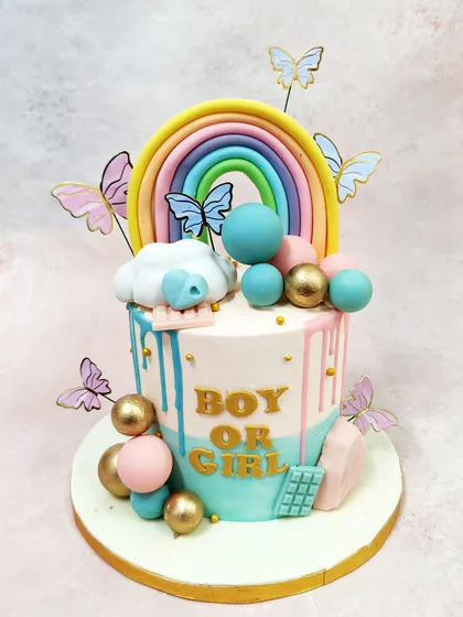 We celebrate new arrivals with this playful and modern gender reveal cake. Drips of pink and blue cascade down the side, while a vibrant rainbow, whimsical butterflies, and decorative spheres in gold, pink, and blue add to the joyful anticipation of discovering if it is a boy or a girl.