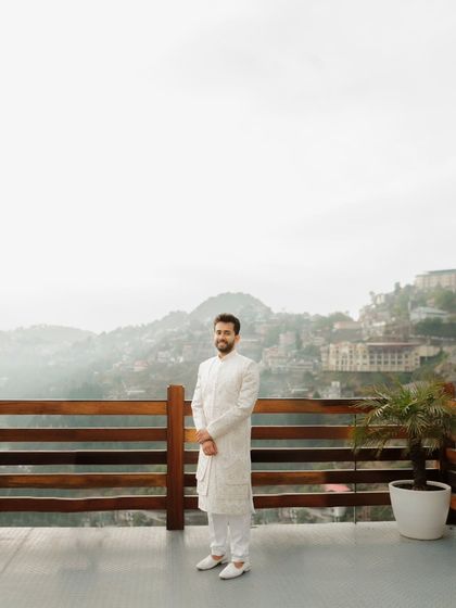 The groom stands alone on a balcony, looking out at the misty Mussoorie hills. This is a quiet, contemplative portrait that captures the anticipation and emotion of the wedding day.