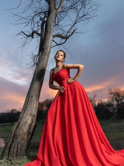 A powerful pose against a sunset sky. This fiery red gown looks absolutely stunning in this artistic pre-wedding shot, creating a dramatic silhouette.