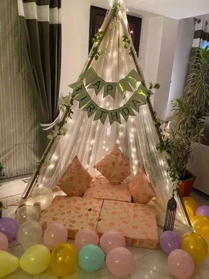 A charming and simple canopy tent setup for a birthday at home. The tent is lit with fairy lights and surrounded by pastel balloons, creating a cozy and cute celebration spot.