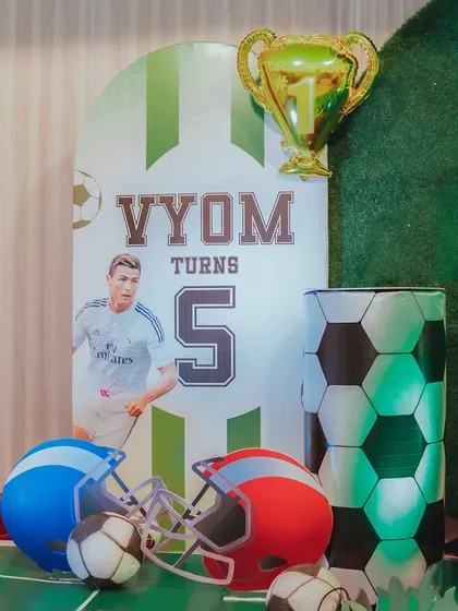 A detailed shot of the football party decor, highlighting the personalized jersey-style sign for "Vyom" and the mix of football and helmet props.