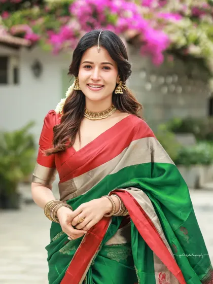 Bright and cheerful outdoor portraits of an actress in a vibrant green and red saree. The natural lighting and blooming flowers in the background complement her radiant smile.