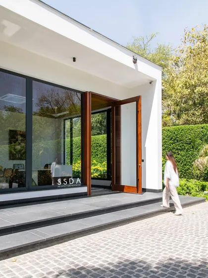 The entrance to The Green Axis office. The design uses large wooden pivot doors and expansive glazing to immediately establish a connection with the lush green hedges and manicured landscape outside.