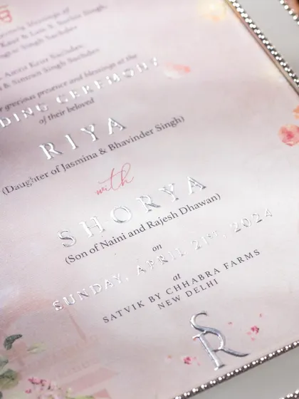 A detailed macro shot of a wedding invitation, focusing on the silver foil-pressed text. This highlights the premium printing technique and luxurious quality of the card.