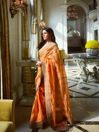 A full-length shot of Nimrat Kaur in a gorgeous orange Torani saree. The entire look is a picture of grace and elegance.