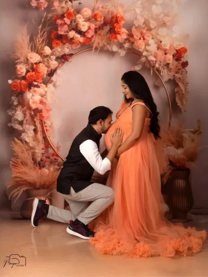 A classic and heartwarming pose. The partner kneels to kiss the baby bump, a beautiful gesture of love and excitement, framed by the boho ring.