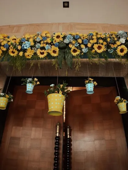 A cheerful and rustic entrance design. I used a combination of bright sunflowers and blue hydrangeas, with hanging floral buckets, to create a welcoming and colorful doorway.