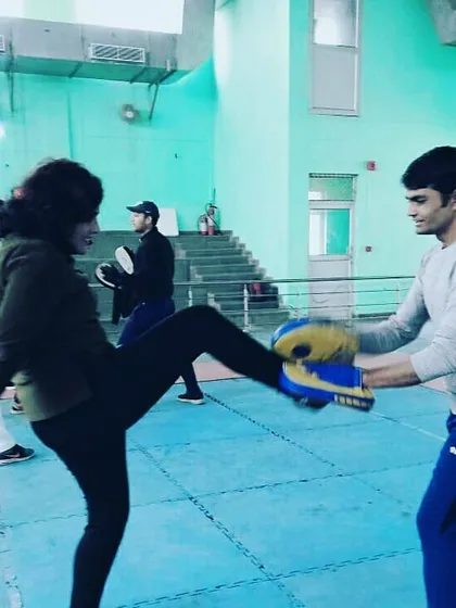 A female student practices a front kick during a self-defence workshop, learning how to use her legs to create distance and disable an attacker.