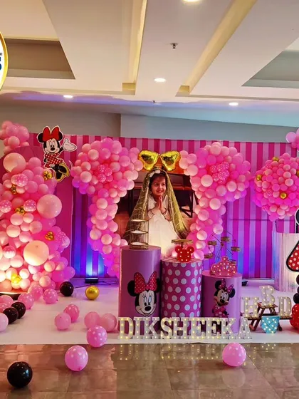 An adorable Minnie Mouse-themed fourth birthday party. This elaborate setup features large, pink, Minnie-shaped balloon sculptures, a striped backdrop, and a photo of the birthday girl.