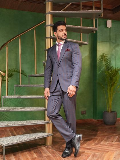 The full-length view of the client's grey suit against a modern staircase. This showcases the complete silhouette and how a bespoke suit can elevate your entire presence.