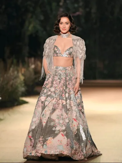 A full-length shot of Shraddha Kapoor walking the ramp. This image showcases the complete outfit, including the fringed cape, and her confident presence.