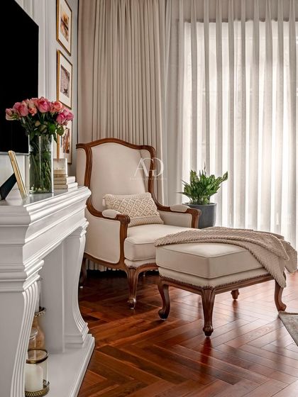 A comfortable reading corner featuring a classic armchair and ottoman set against a backdrop of rich, dark wood flooring. The nearby fireplace adds to the cozy and inviting ambiance.