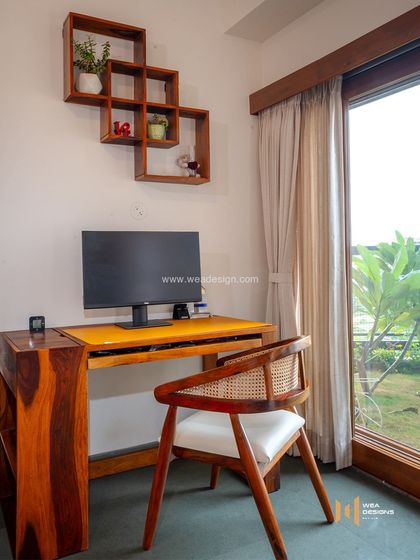 A simple and serene study corner in the Total Environment project, featuring a solid wood desk and chair overlooking a garden, perfect for focused work.