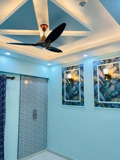 A bedroom with a cool blue color scheme, featuring a wardrobe with a geometric-patterned laminate and framed wallpaper panels on the wall.
