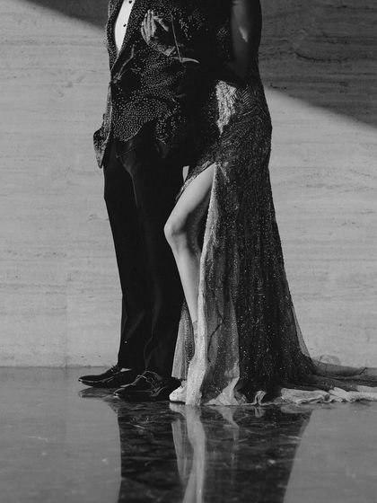 A dramatic black and white shot of the couple's Sangeet look. The focus on the texture of their outfits and their confident poses creates a powerful and stylish image.