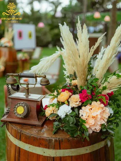 A charming decor detail for a boho-themed Mehendi, featuring a vintage telephone on a rustic barrel, adorned with flowers.
