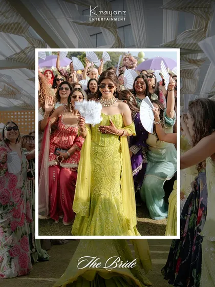 The bride, surrounded by her friends holding traditional fans, makes a grand entrance at her Mehendi. She is the center of attention and glowing with happiness.