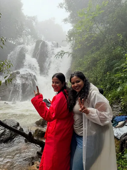Two trekkers flashing victory signs in front of a waterfall on the Bandaje trek. The joy of reaching these beautiful spots is immense.