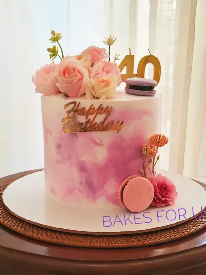 A stylish 40th birthday cake with a pink watercolor effect, decorated with fresh flowers and macarons. A chic and modern design for a milestone celebration.