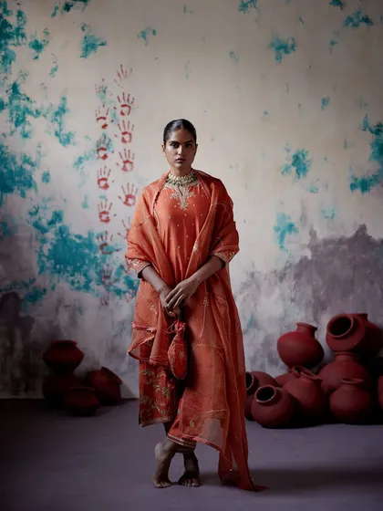 An earthy orange kurta set with a matching potli bag. The intricate embroidery and rich colour make it a warm and inviting choice for any festive gathering.