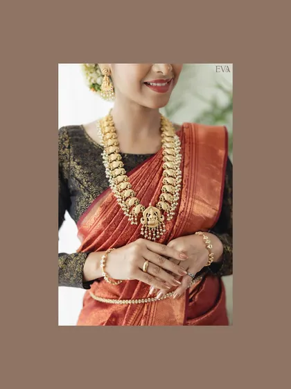 A medium close-up focusing on the stunning antique gold necklace against the rust-colored saree. This shot is perfect for jewellery designers and catalogues.