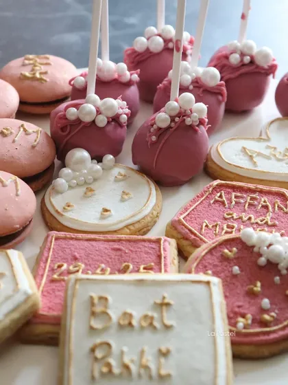 It's all in the details. 🫶🏻 Look at this close-up of the custom treats, including hand-piped cookies with the couple's names and date, pretty pink cake pops, and initialed macarons.