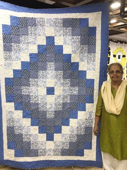 A client proudly displaying her large blue and white "Trip Around the World" quilt.