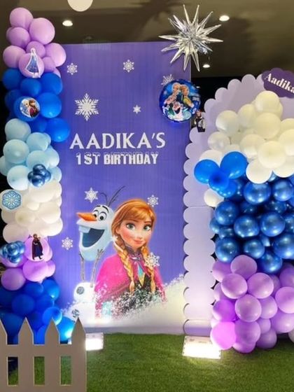 A detailed look at a Frozen first birthday backdrop, combining balloon columns, character prints, and a picket fence for a charming photo corner.