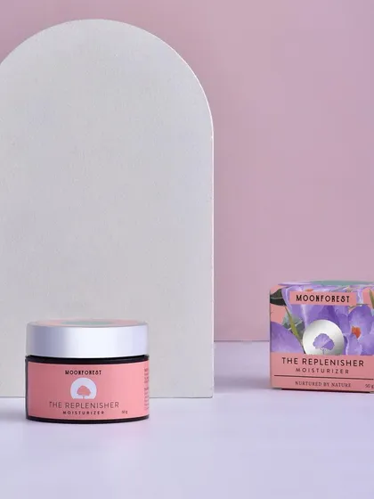 A minimalist shot of Moon Forest's moisturizer and its packaging. The simple background and props keep the focus entirely on the product's branding and design.