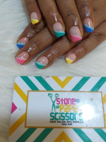 A fun and colorful French tip design on short, natural nails. Each tip is painted a different bright color, separated from the nude base by a thin silver glitter line.