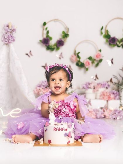 A happy little girl enjoying her first birthday cake. The butterfly theme in shades of purple is so whimsical and sweet.