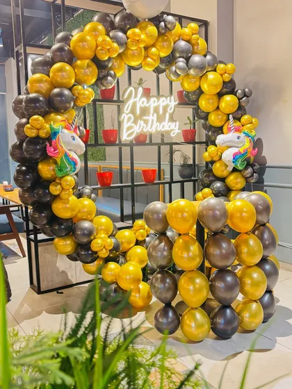 A unique unicorn-themed birthday setup with a black and gold circular balloon arch and a neon sign.