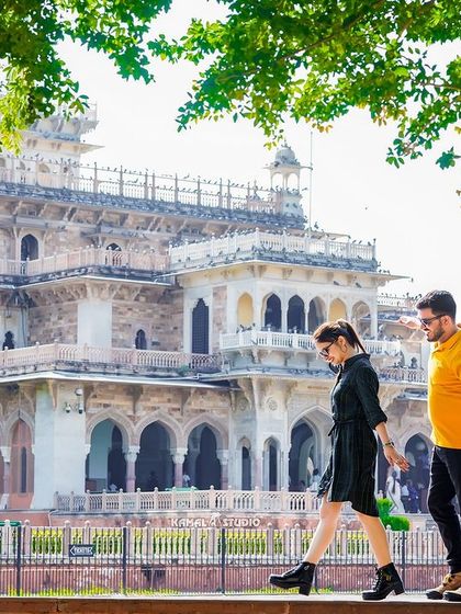 A stylish, candid shot of the couple walking along a wall with the Albert Hall Museum in the background, showcasing a modern, casual vibe in a historic setting.
