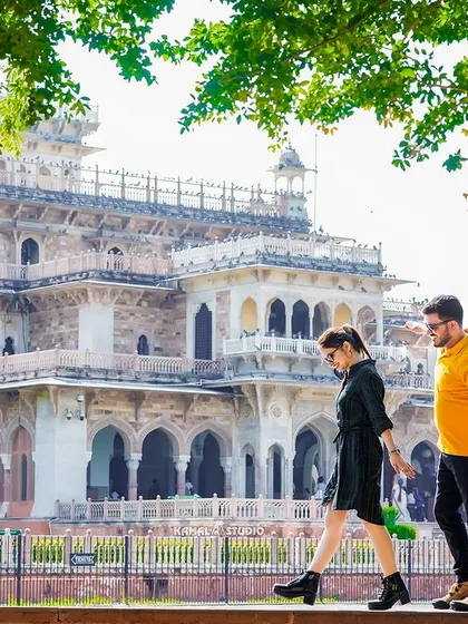 A stylish, candid shot of the couple walking along a wall with the Albert Hall Museum in the background, showcasing a modern, casual vibe in a historic setting.