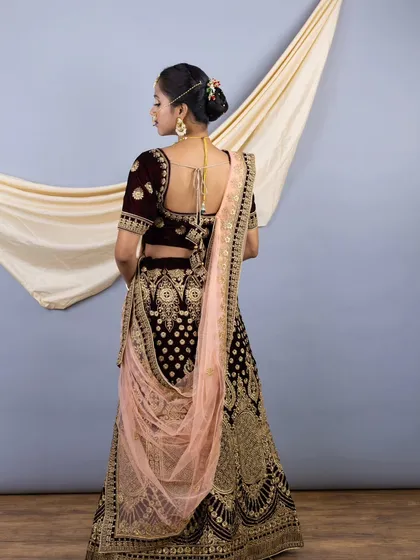The back view of the wine velvet bridal lehenga, showing the deep back of the blouse and the elegant drape of the pastel pink dupatta.