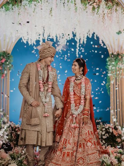The couple stands together at their beautiful mandap, showered in confetti. A perfect, happy portrait that encapsulates the joy of the wedding ceremony.