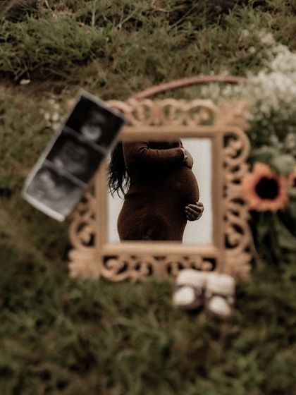 An artistic flat lay in the grass, using a mirror to reflect the baby bump, surrounded by sonogram pictures and baby shoes. This is a highly creative and visually interesting announcement shot.