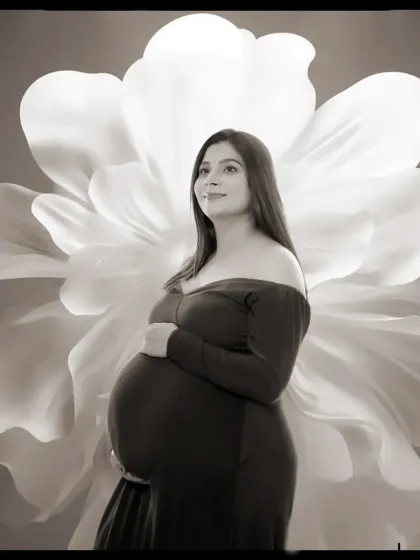 A hopeful black and white portrait of a mother-to-be looking towards the light, with a large floral prop creating a beautiful silhouette behind her.