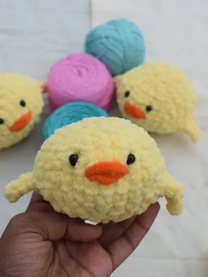 Holding one of my chick plushies up close to show its soft texture and cute face. Behind it, you can see more of the flock and the colorful yarn I use.