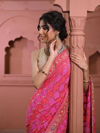 A joyful moment captured. The model's smile complements the vibrant pink of the bandhani saree, showcasing the intricate border and the elegant drape.