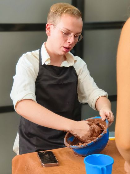 A traveler learns the first step of pottery: mixing clay. We provide an immersive, hands-on experience for those looking to connect with local art forms.
