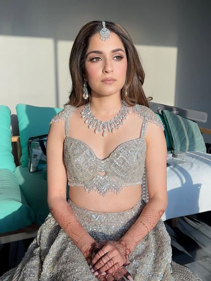 A full-length view of the bride seated. The cool tones of the silver lehenga are balanced by the soft warmth in the makeup, creating a look that is harmonious and elegant.