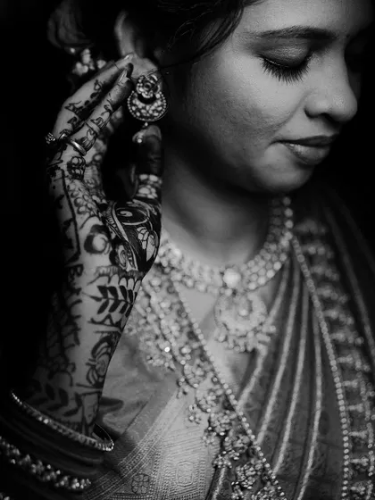 A stunning black and white bridal portrait focusing on the intricate details of the bride's mehndi and jewelry. The lighting creates a soft, dramatic mood.