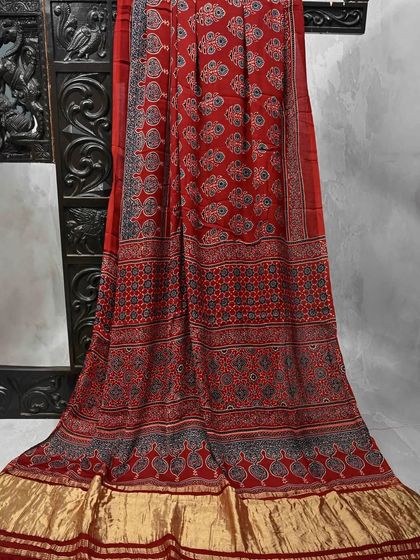 A rich red Ajrakh printed saree with a contrasting gold border. This piece is a perfect blend of traditional craft and festive elegance.