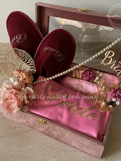 A hamper fit for a queen. This luxurious velvet box for the bride is filled with a personalized satin robe, matching slippers, and a custom "Bride" prop for photos, ensuring she feels like royalty.